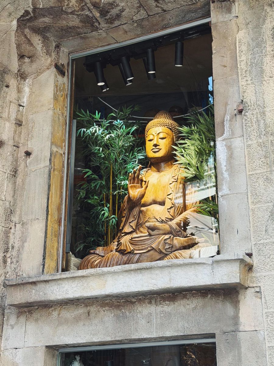 Goldene Buddha-Statue mit erhobener Hand zwischen Bambus hinter einem Fenster in einer alten Steinfassade